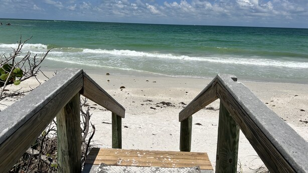 A wooden staircase leading to a sandy beach with ocean waves in the background.