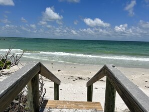 A wooden staircase leading to a sandy beach with ocean waves in the background.