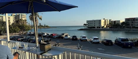 A balcony with a view of a marina, parked cars, and buildings along the waterfront.