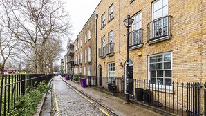 A narrow cobblestone street lined with brick buildings, featuring a black metal fence and a row of trash bins. - Paradise Row Townhouse (London)
