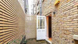 A narrow alleyway with a wooden fence on one side and a brick wall on the other. A white door is visible in the center. - Paradise Row Townhouse (London)