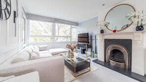 Un salon moderne avec un canapé d’angle, une cheminée, un téléviseur posé sur un meuble et de grandes fenêtres.
