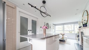 Une cuisine moderne dotée d’un îlot central, de meubles blancs et d’une grande fenêtre qui laisse entrer la lumière naturelle.