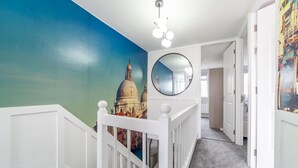Un couloir avec une rambarde blanche, un miroir rond et une fresque représentant un bâtiment.