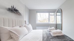 Une chambre moderne avec un grand lit, un radiateur, une fenêtre donnant sur un beau paysage et un miroir.