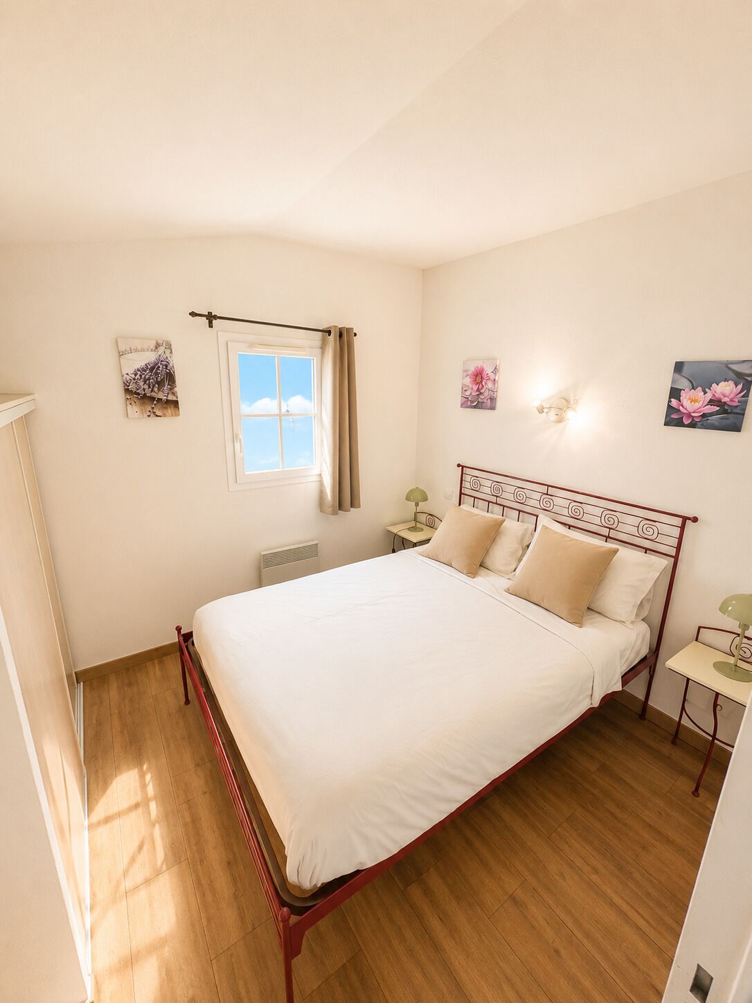 Une chambre à coucher avec un lit, une fenêtre avec des rideaux, une table de chevet, une lampe et des œuvres d’art murales.