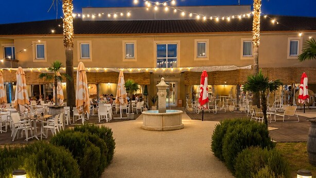 A hotel courtyard with outdoor seating, palm trees, and a fountain. - Hôtel Restaurant Les Jasses de Camargue (Gallargues-le-Montueux)
