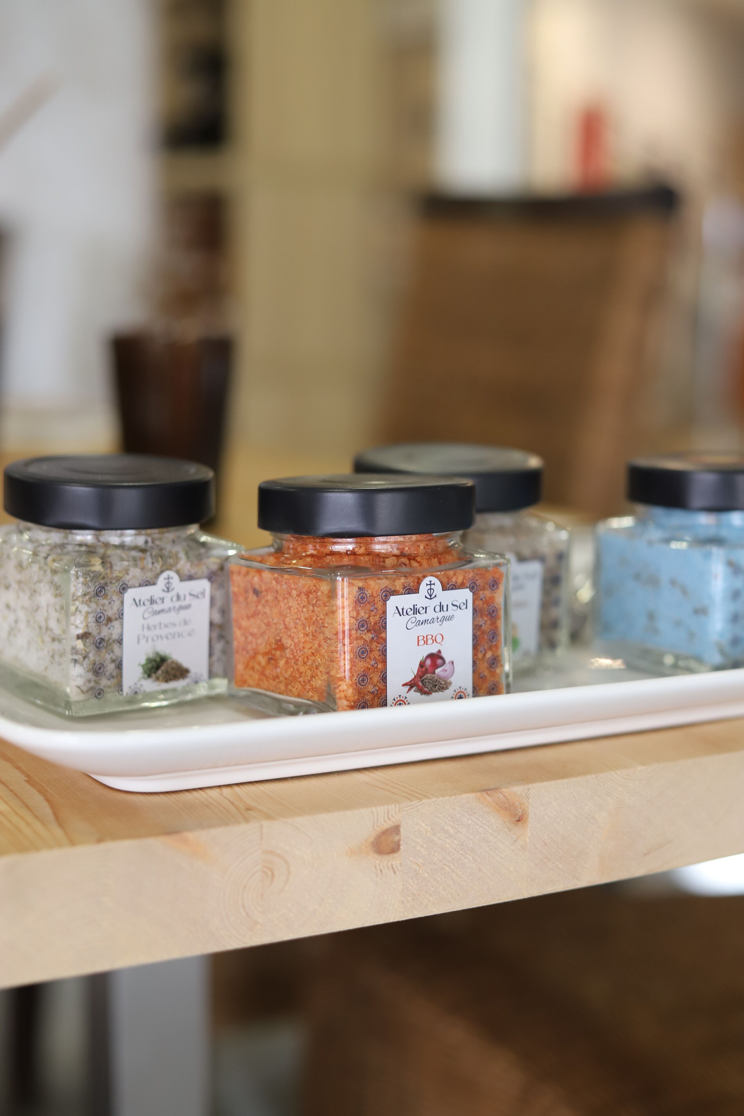 A tray with four glass jars of different herbs and spices, each with a black lid and labeled with their names and origins.