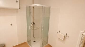 A modern bathroom with a glass-enclosed shower, a toilet, a small potted plant, and a towel rack.