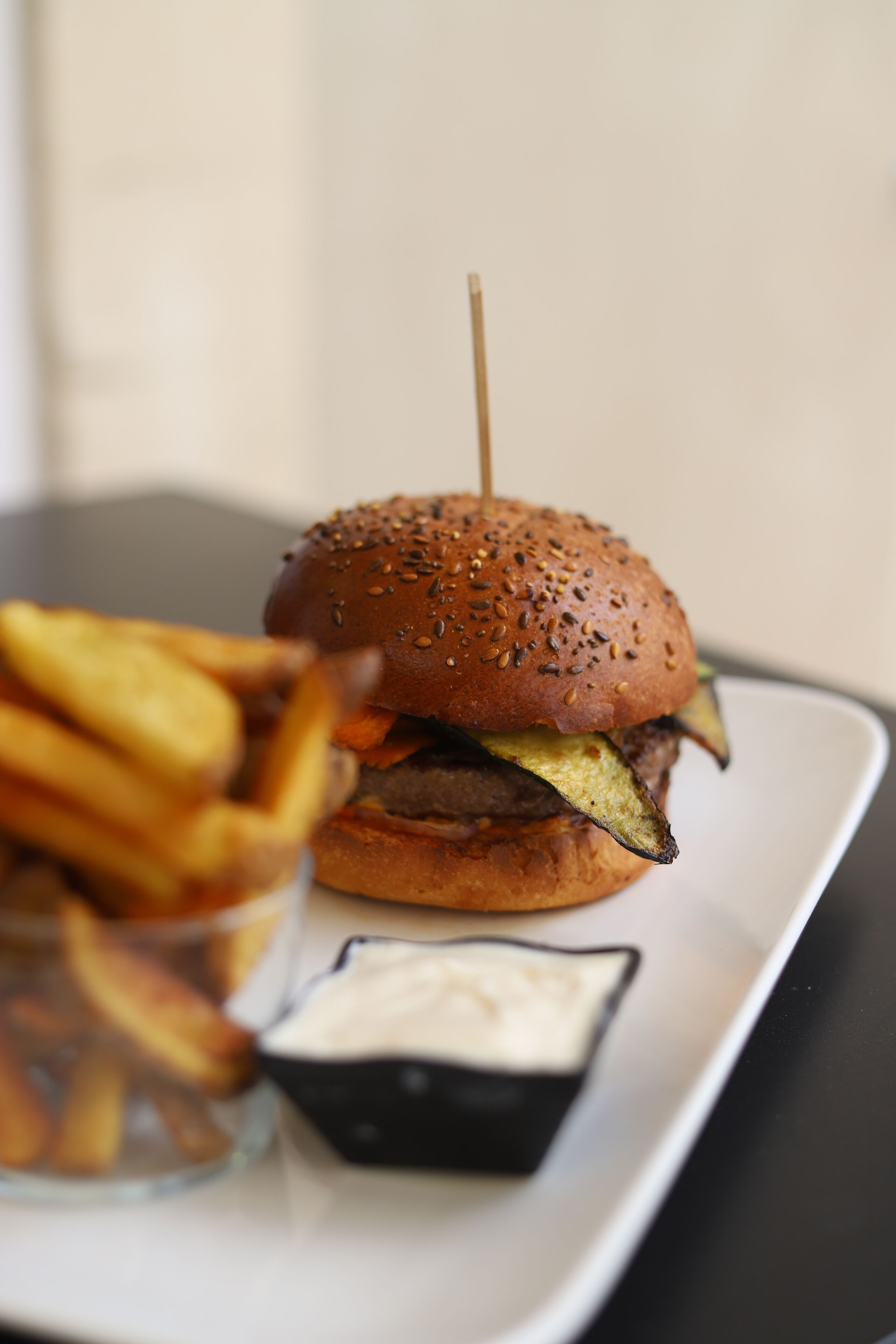 Ein Burger mit Pommes und einer kleinen Soßenportion auf einem weißen Teller.