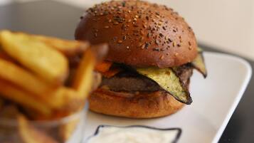 A burger with fries and a small container of sauce on a white plate.