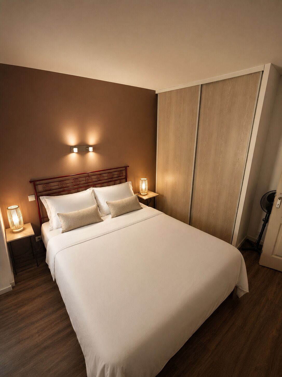 A hotel room with a large bed, two bedside lamps, a wooden headboard, and a wardrobe.