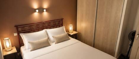 A hotel room with a large bed, two bedside lamps, a wooden headboard, and a wardrobe.
