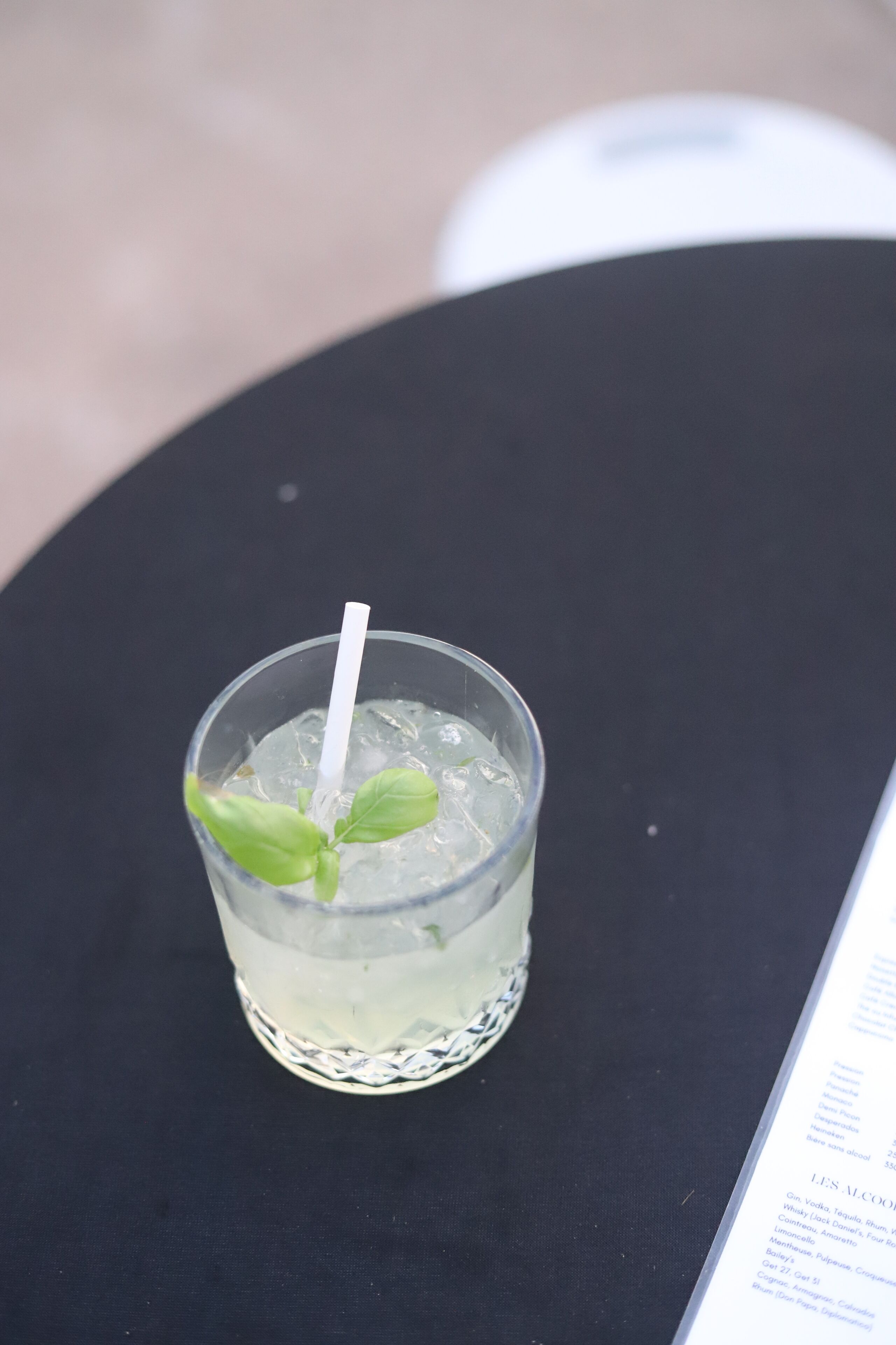 A glass of water with a straw and mint leaves on a black table.