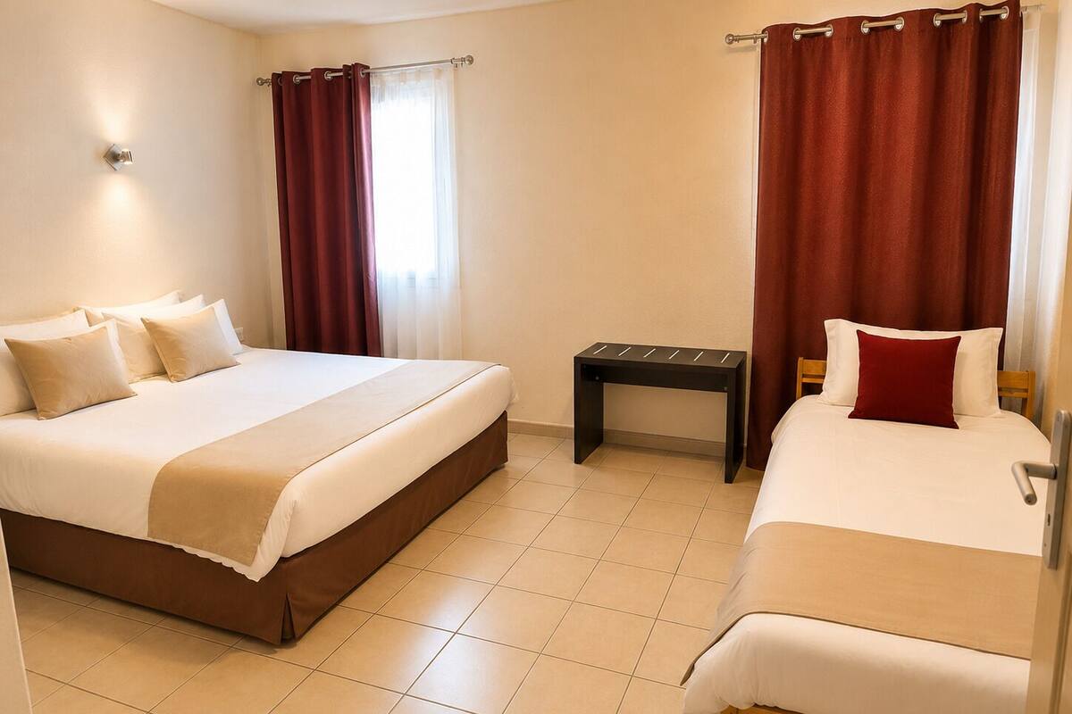 A hotel room with two beds, a small table, and a window with curtains.