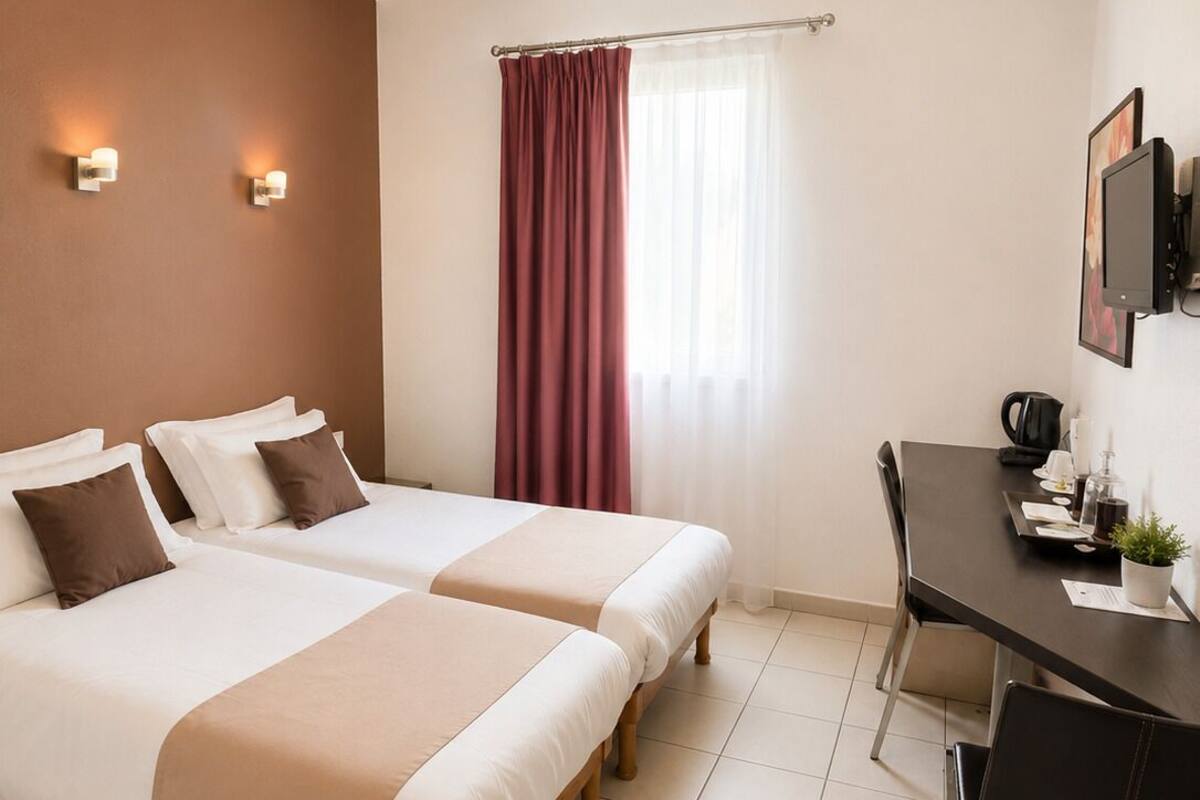A hotel room with two beds, a desk, a chair, a television, and a window with curtains.