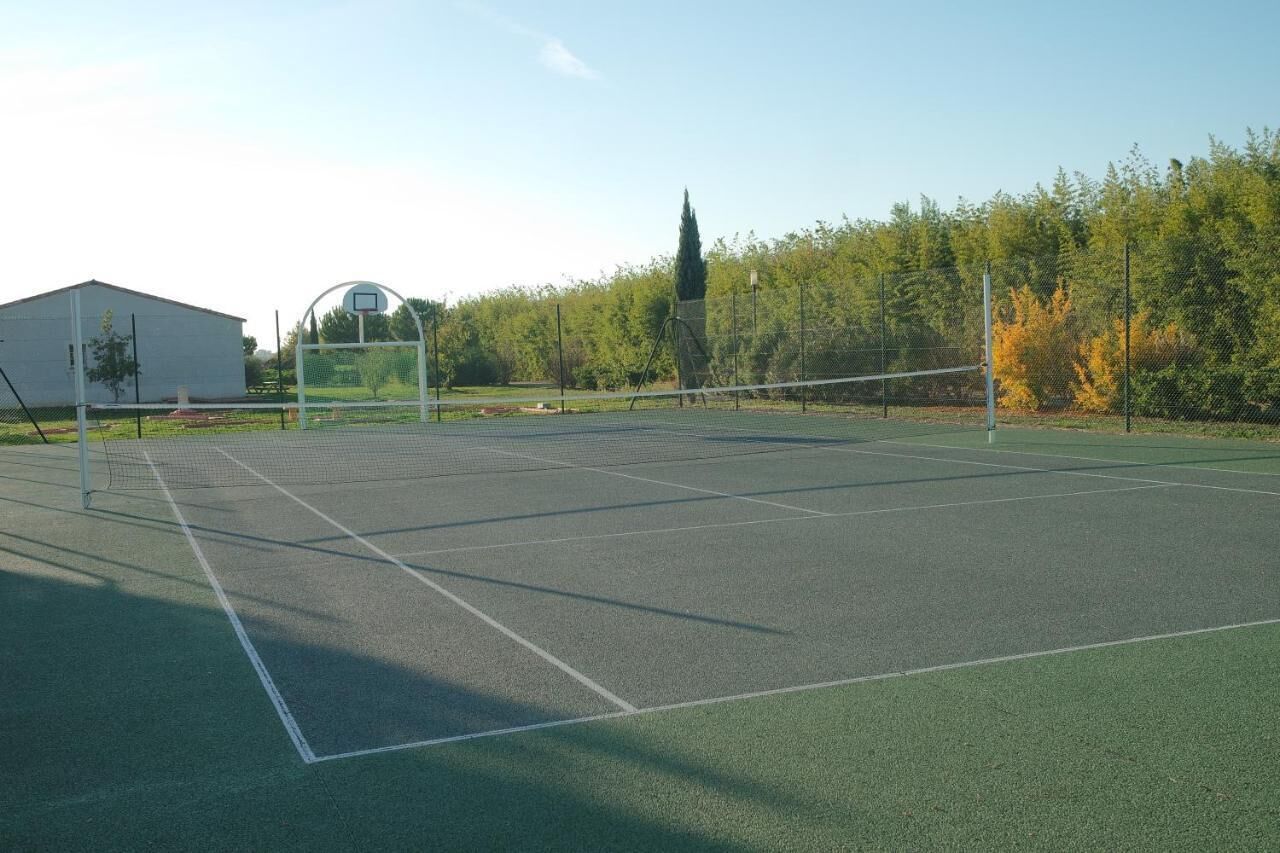 An outdoor tennis court with a net, surrounded by trees and a building.
