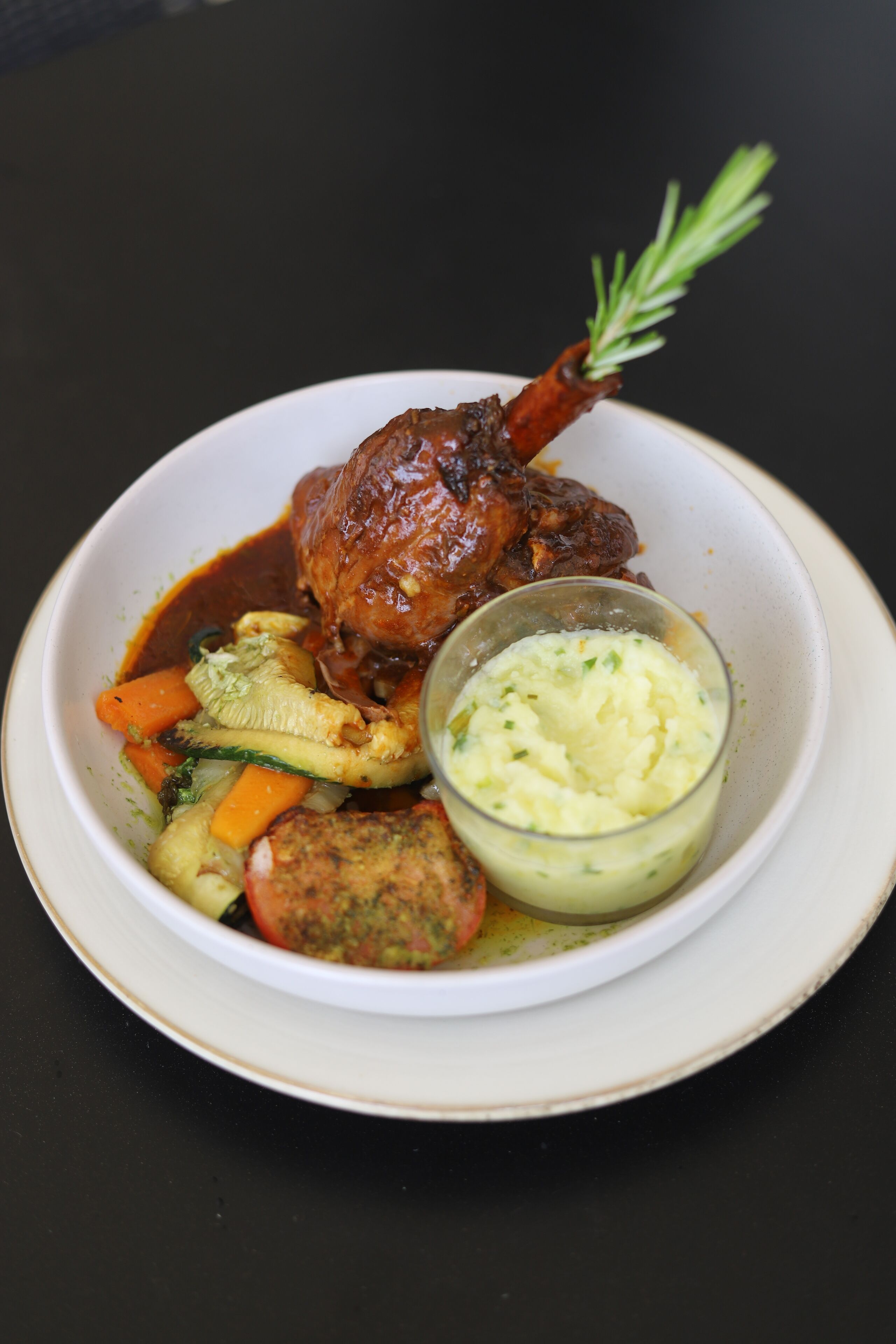 A plate with a roasted leg of lamb, vegetables, and a side of mashed potatoes.