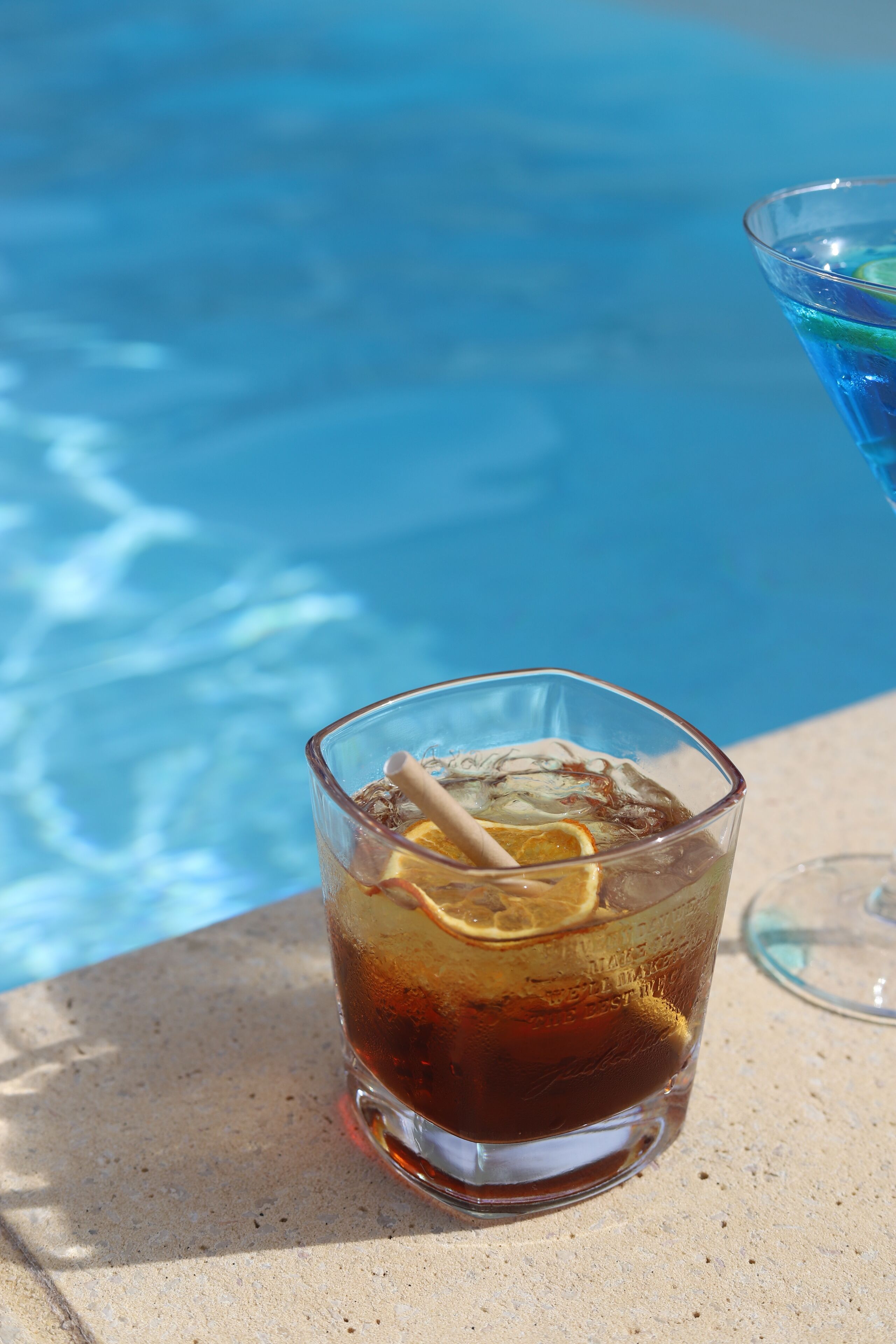 A glass of iced tea with lemon slices and a straw by a poolside.
