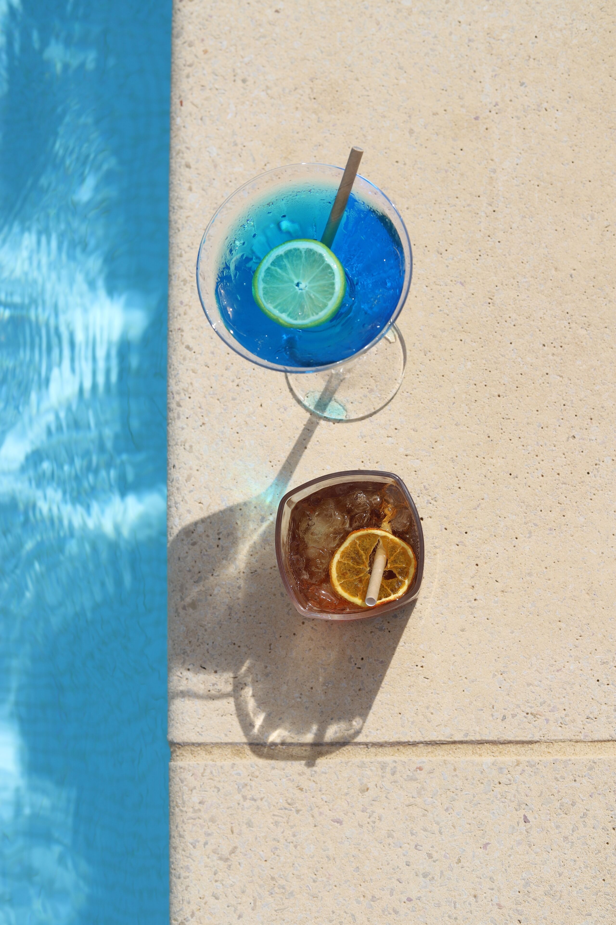 Zwei Getränke auf einer Betonfläche in der Nähe eines Pools.