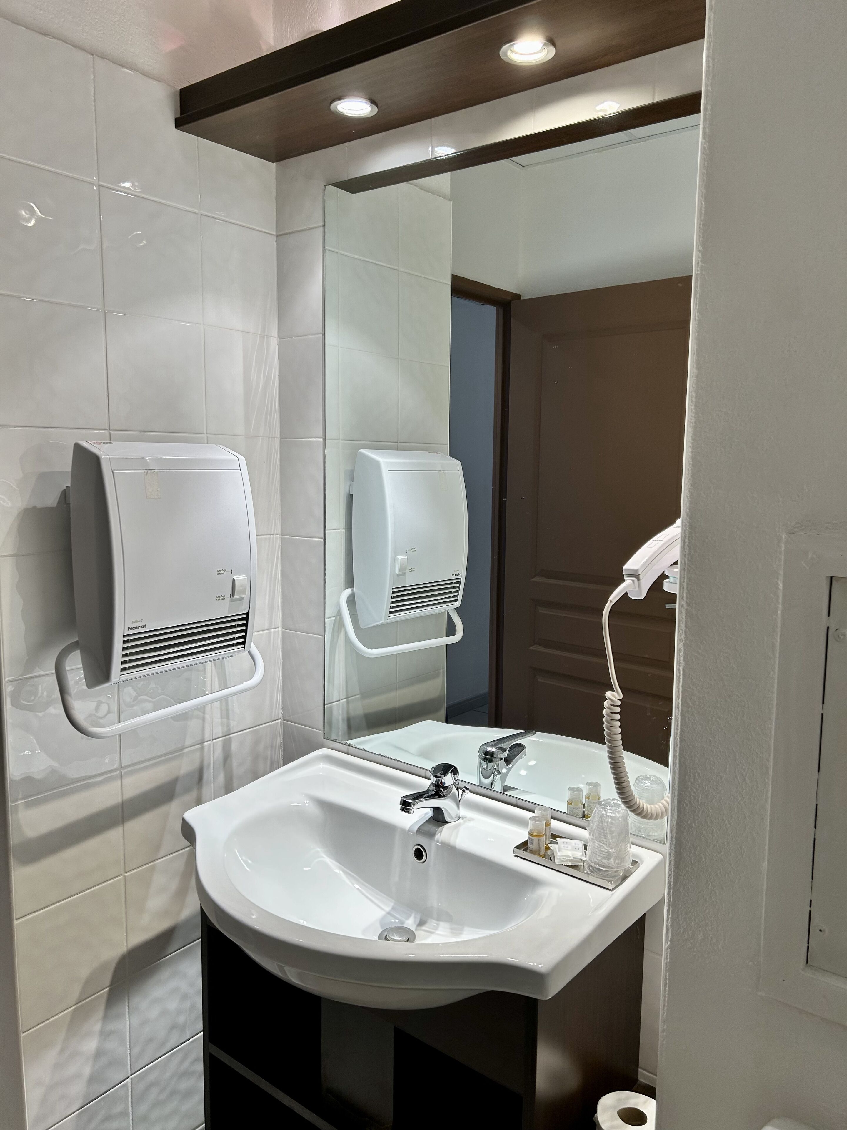 A modern bathroom with a white sink, two hand dryers, and a mirror.