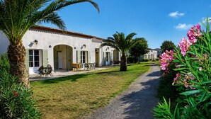 A building with a paved pathway, outdoor seating, and a palm tree. - Hôtel Restaurant Les Jasses de Camargue (Gallargues-le-Montueux)