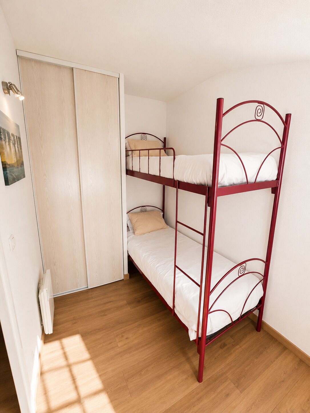 A bunk bed with a wooden floor, a white door, and a light switch.