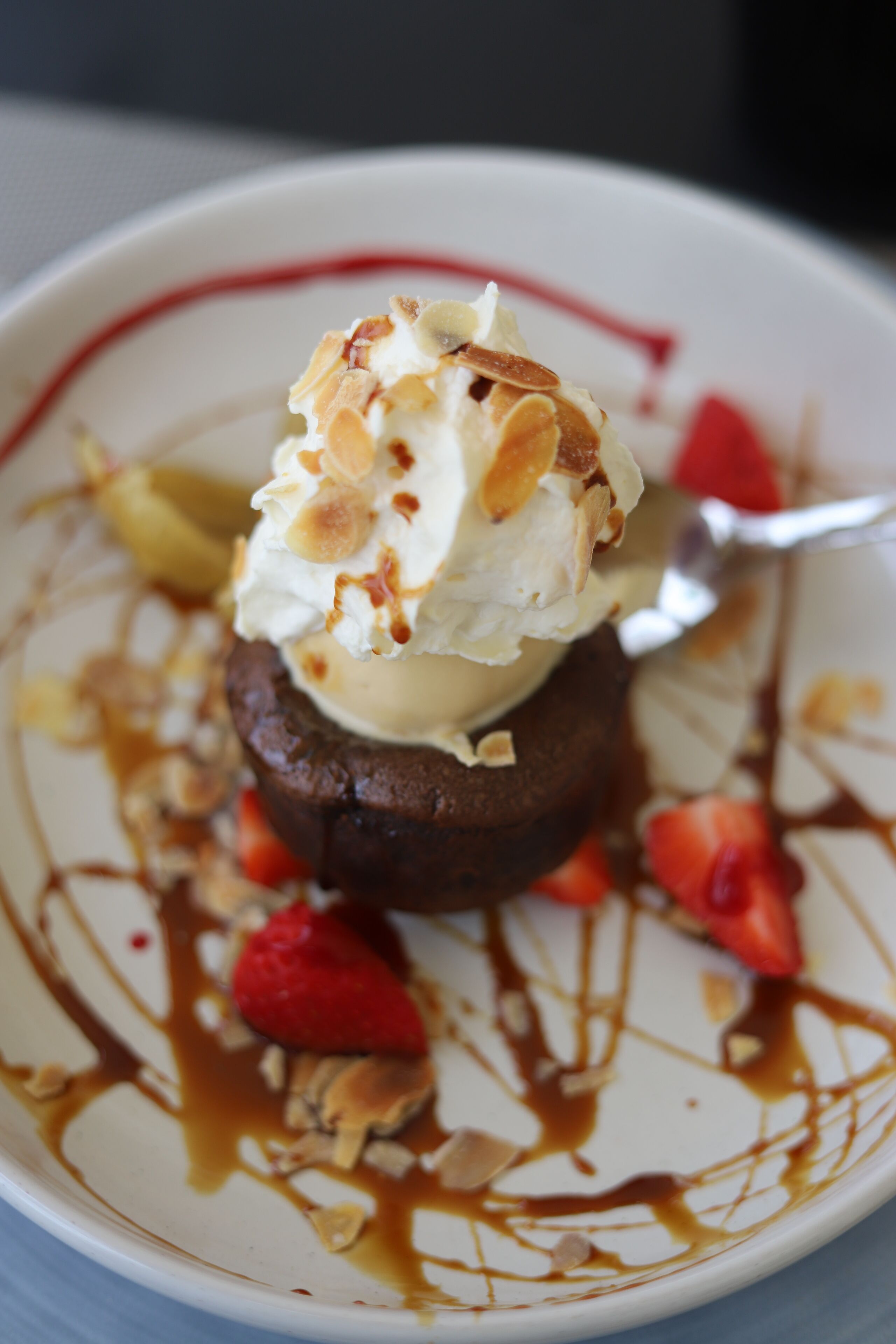 Un postre con una bola de helado encima, rodeado de fresas y bañado en salsa de caramelo.