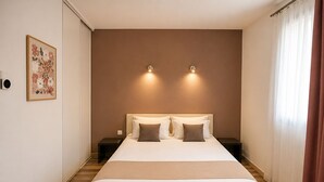 A bedroom with a large bed, two bedside tables, a wall-mounted light fixture, and a window with curtains. - Hôtel Restaurant Les Jasses de Camargue (Gallargues-le-Montueux)