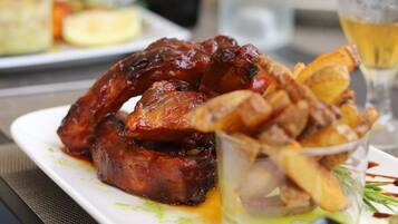 A plate of ribs and fries with a small bowl of sauce, a glass of beer, and a bottle of water on a table.