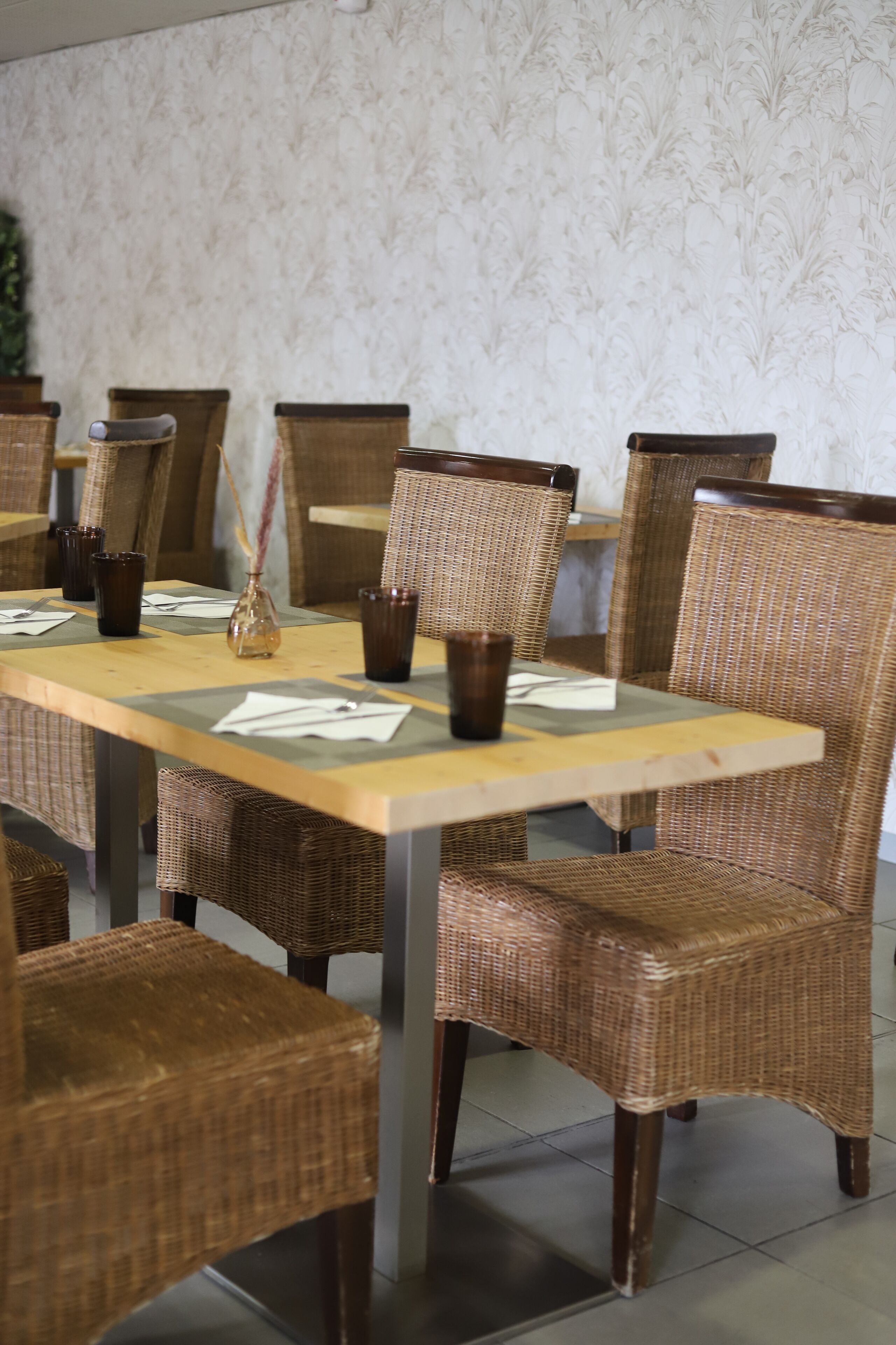 A dining area with wicker chairs and a table set with napkins, a vase, and a candle.
