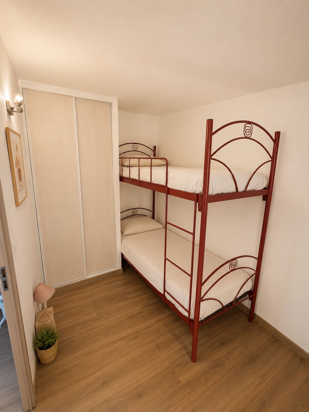 A bunk bed in a room with wooden flooring, a door, and a small plant.