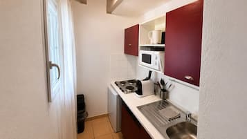 Een praktische keuken met een magnetron, fornuis, spoelbak en een kleine koelkast.