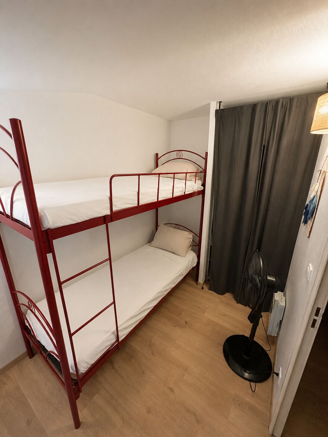 Egy emeletes ágyas szoba mennyezeti ventilátorral és egy függönnyel ellátott ajtóval.