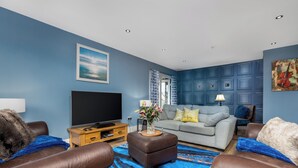 Una sala de estar con un televisor de pantalla plana, un sofá gris, sillones de cuero marrón y un tapete azul estampado.