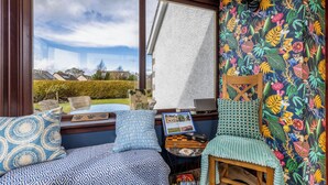 Una habitación acogedora con un ventanal grande, una computadora portátil sobre una mesita y una silla.