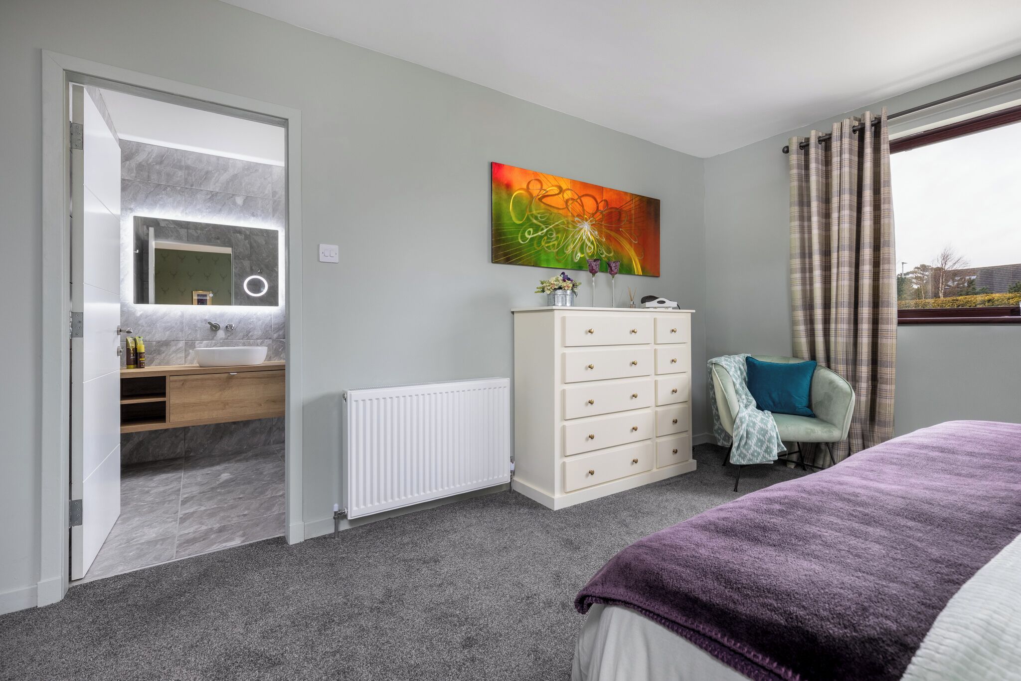 Een slaapkamer met een bed, een kaptafel, een spiegel, een radiator en een raam met gordijnen.