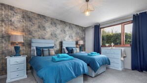 Un dormitorio con dos camas, una mesita de noche con lámpara, un aparador y una ventana con cortinas.