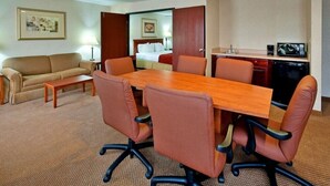 A hotel room with a wooden dining table, six brown chairs, a sofa, a small coffee table, a kitchenette with a microwave, and a bed with a nightstand. - Seasons Inn Suites Highland (Highland)