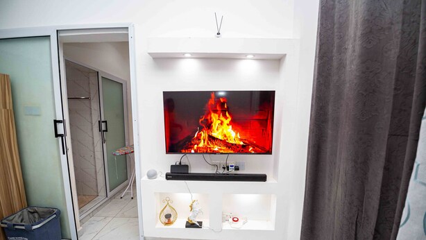 Un salon moderne avec un téléviseur à écran plat fixé sur un mur blanc, une petite étagère ornée d’objets décoratifs et une porte coulissante donnant sur une autre pièce.
