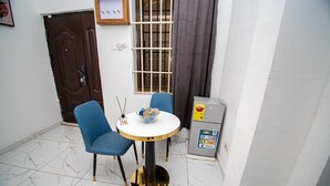 Un petit coin repas avec une table ronde, deux chaises bleues, un bol décoratif et un réfrigérateur.