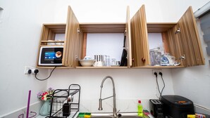 Une cuisine compacte équipée d’un four à micro-ondes encastré, d’un évier et de placards en bois situés au-dessus.