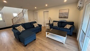 A spacious living room with two dark blue sofas, a wooden coffee table, and a staircase leading to another level. - Ocean view cottages with direct beach access (Savage Harbor)