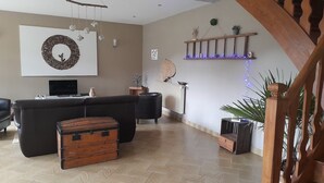 Un salon comprenant un grand canapé d’angle, une commode en bois et une étagère murale agrémentée d’objets décoratifs.