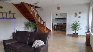 Un salon avec un canapé en cuir marron, un escalier en bois et une cuisine à l’arrière-plan.