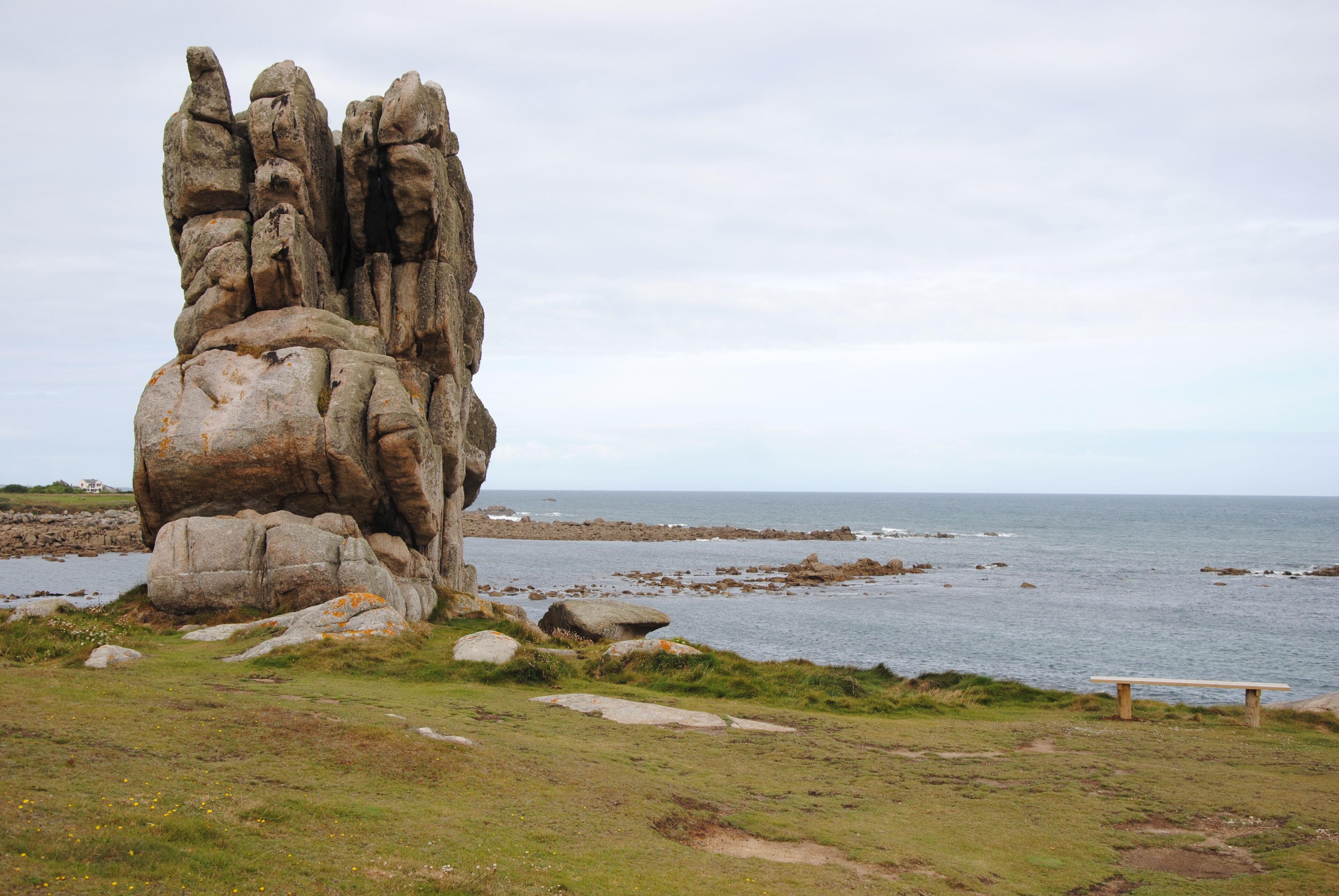 Un paisaje costero con una roca destacada, una zona con césped y un banco.