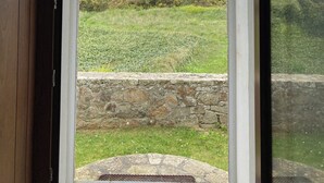 Un portail en arc donne accès à un espace verdoyant, bordé d’un mur de pierre, d’où l’on peut admirer la mer.