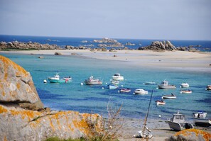 Vista costera con barcos anclados cerca de una playa arenosa y afloramientos rocosos.