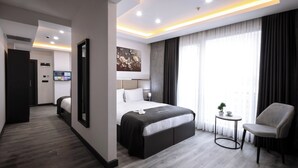 A modern hotel room with a large bed, a seating area, and a television. - Meyzi Hotel (Arnavutköy)