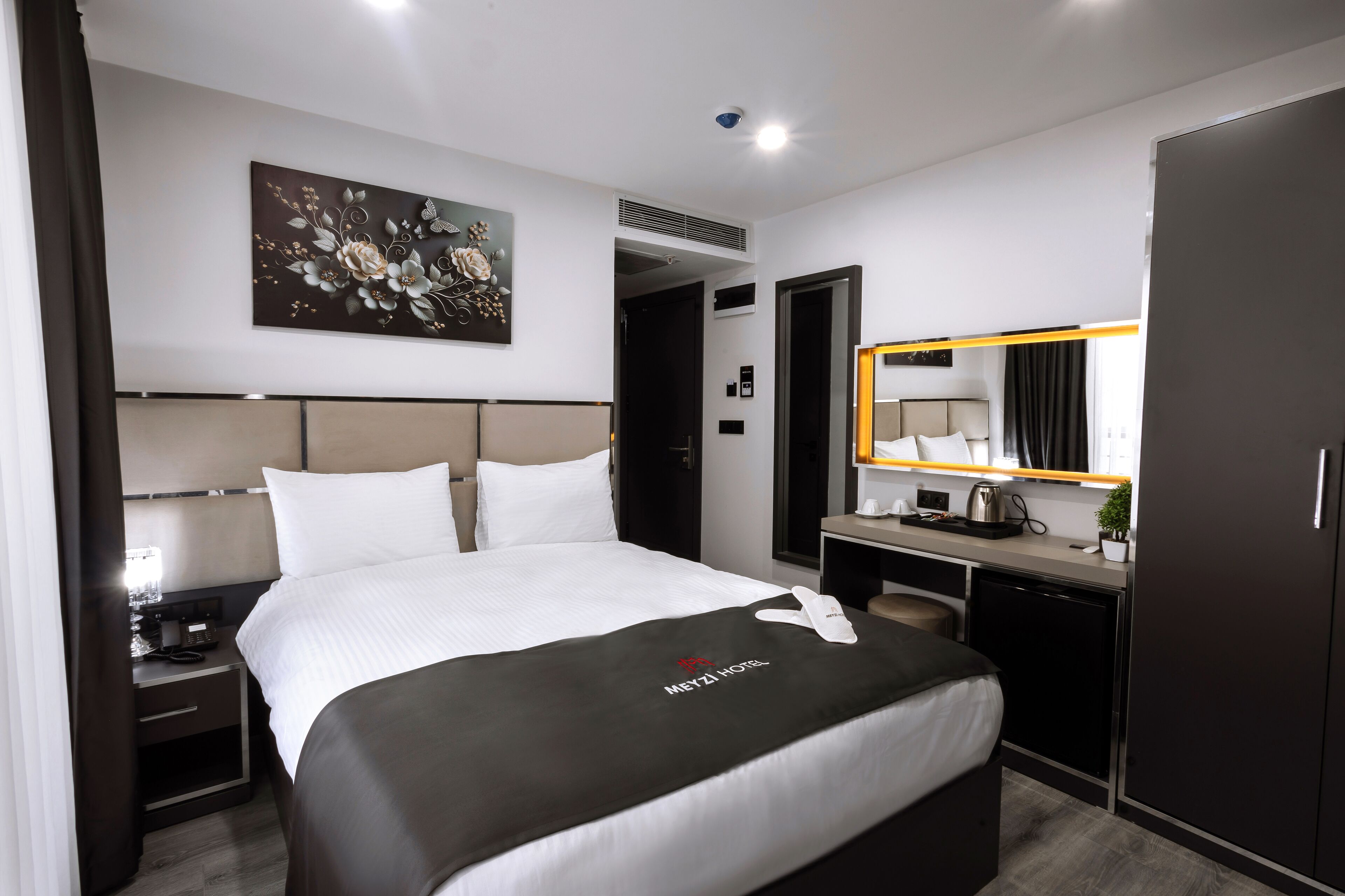 A hotel room with a bed, bedside table, lamp, and a large mirror.